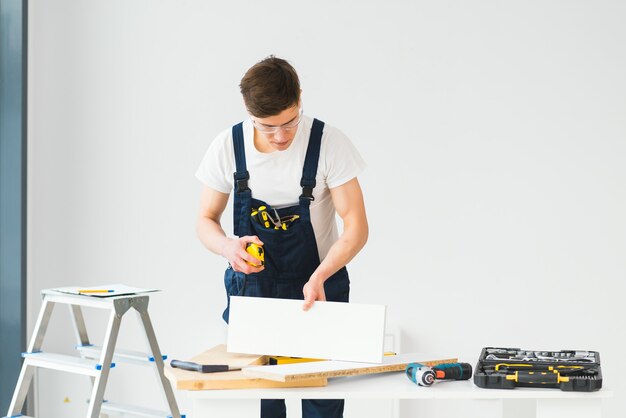 Reparatur-, Bau- und Gebäudekonzept - glücklich lächelnder männlicher Arbeiter oder Baumeister in der Schutzbrille am neuen Haus auf Hintergrund