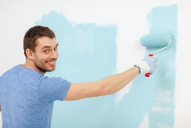 Foto reparatur-, bau- und hauskonzept - lächelnder mann, der zu hause wand malt