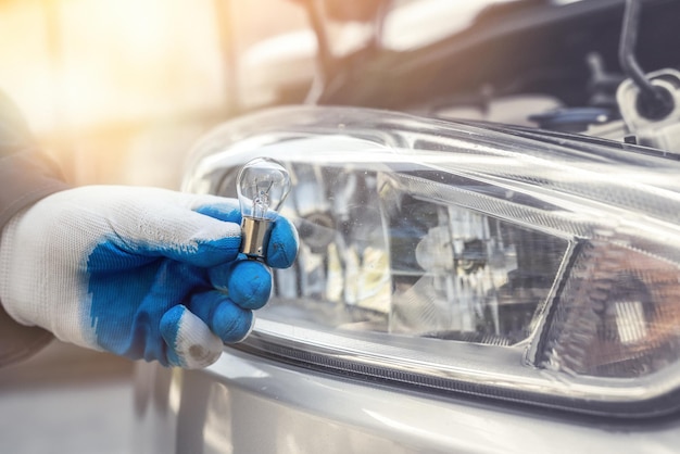 Reparatur, die Glühbirne des neuen Autos unter Täuschung für Scheinwerfer hält, Auto als Hintergrund. Nahansicht