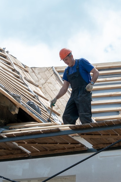 Reparatur eines alten Holzdaches Austausch von Ziegeln und Holzbalken in einem alten Haus Ein Zimmermann mit Werkzeugen in den Händen ist während der Arbeiten auf dem Dach des Gebäudes