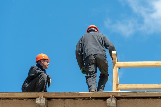 Reparatur eines Holzdaches im Freien vor blauem Himmel Zwei Zimmerleute in Spezialkleidung arbeiten in einer Höhe Dachdecker bereiten das Dach für die Installation der Isolierung vor