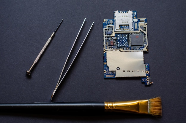 Reparatur von Mobiltelefonen und verschiedenen elektronischen Geräten Der Chip des elektronischen Geräts liegt auf schwarzem Hintergrund auf dem Tisch