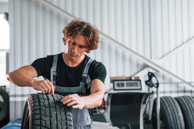 Repariert kaputte Reifen Erwachsener Mann in grauer Uniform arbeitet im Autosalon