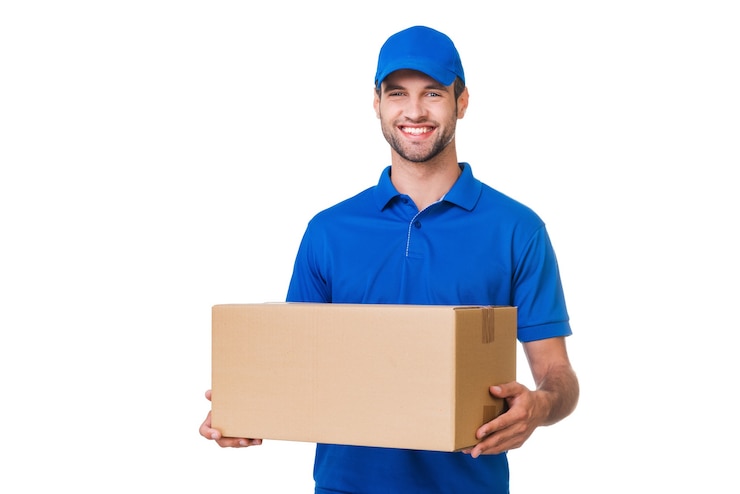 Foto repartidor alegre. mensajero joven feliz sosteniendo una caja de cartón y sonriendo mientras está de pie contra el fondo blanco.