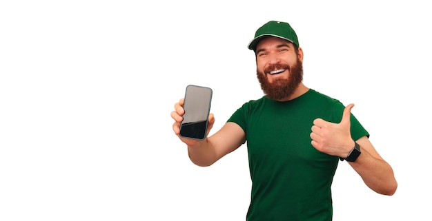 El repartidor alegre de verde muestra la pantalla de su teléfono y un pulgar hacia arriba