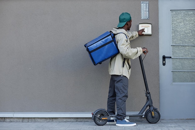 Repartidor de alimentos tocando el timbre mientras conduce scooter eléctrico