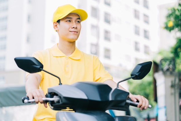 Repartidor asiático está conduciendo su motocicleta para entregar al cliente