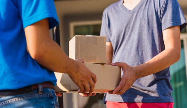 Repartidor asiático joven con buzón de paquetes en uniforme máscara protectora que hace el servicio y el cliente recibe la casa bajo toque de queda cuarentena pandemia coronavirus COVID-19