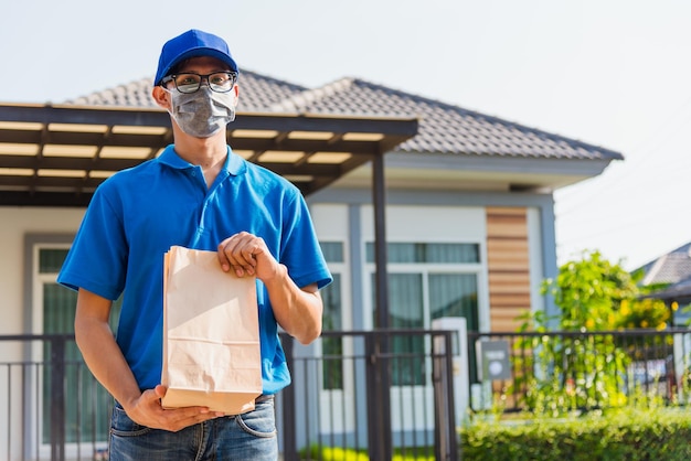 Repartidor asiático joven repartidor en línea con pedidos de comida para llevar contenedores de bolsas de papel con máscara protectora, servicio al cliente en la casa bajo toque de queda cuarentena pandemia coronavirus COVID-19