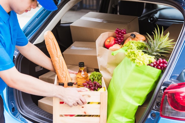 El repartidor asiático prepara el servicio de comestibles dando verduras frescas, comida y fruta llenas en una cesta de madera en el camión trasero para enviar a la mujer a la puerta de su casa después del coronavirus pandémico, Volver a la nueva normalidad