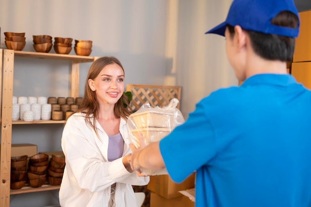 Un repartidor asiático con uniforme azul que envía comida a una joven cliente en su tienda