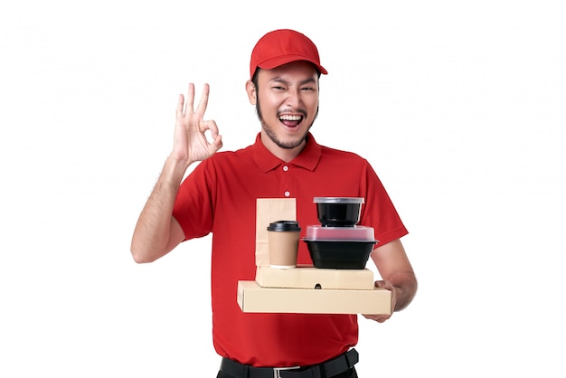 Repartidor asiático con uniforme rojo con caja de almuerzo y café para llevar aislado sobre fondo blanco. servicio de entrega urgente durante covid19.