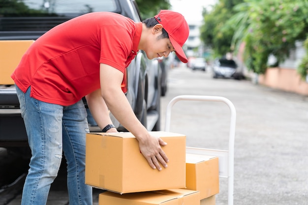 Repartidor asiático con uniforme rojo y sombrero rojo en movimiento y transferencia de cajas de paquetería.