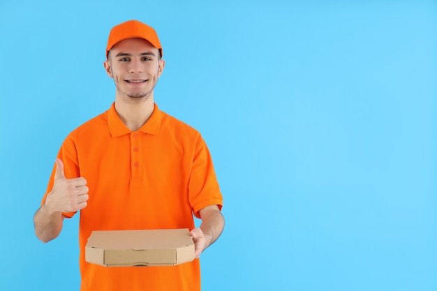 Repartidor atractivo con caja de pizza sobre fondo azul.