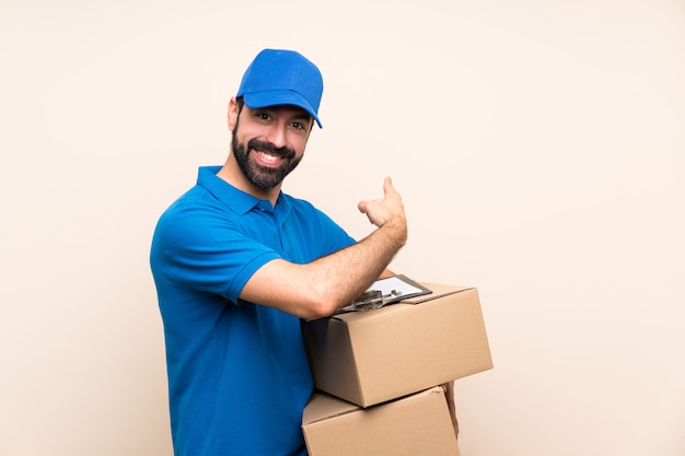 Repartidor con barba sobre pared aislada apuntando hacia atrás