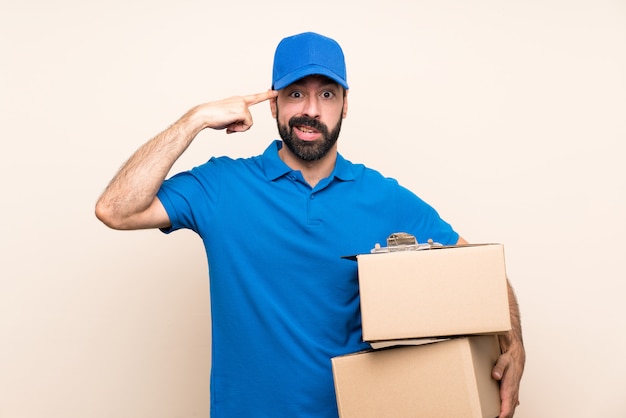 Repartidor con barba sobre pared aislada haciendo el gesto de locura poniendo el dedo en la cabeza