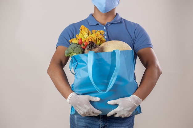 Repartidor con bolsa de frutas y verduras con mascarilla y guantes