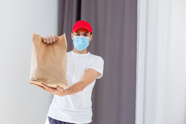 Repartidor con bolsa de papel con comida sobre fondo blanco, repartidor de alimentos en máscara protectora