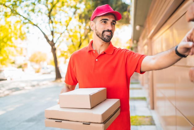 Foto repartidor con caja de pizza tocando el timbre de la casa.