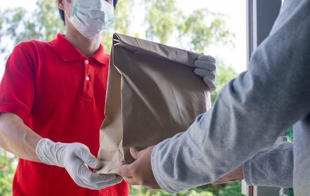 Repartidor en camiseta roja uniforme máscara facial guantes sostener bolsa de papel Cliente que recibe el pedido del servicio de mensajería en el hogar Servicio durante la cuarentena 2019ncov concepto de coronavirus