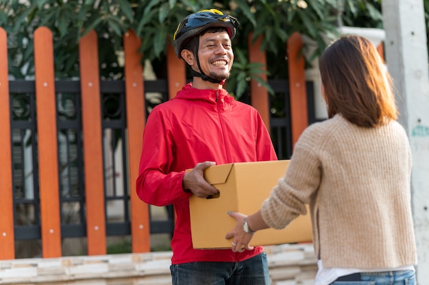 Repartidor dando cajas a mujeres jóvenes en casa, concepto de servicio de mensajería