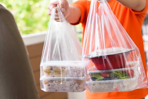 Repartidor dando comida de caja de almuerzo en las bolsas a cutomer que ordenó en línea en casa