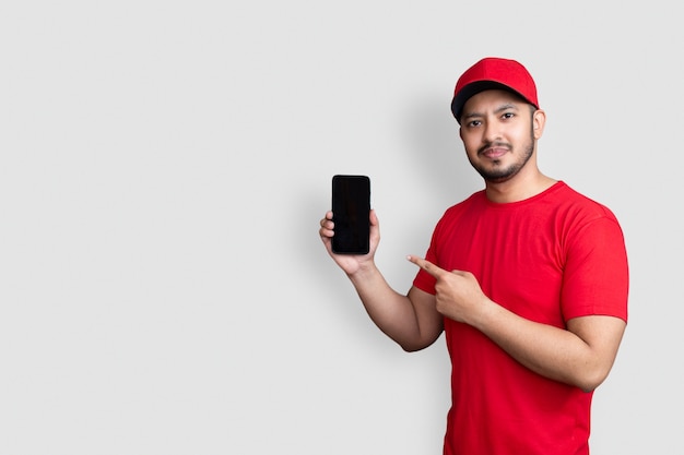 Repartidor empleado en gorra roja camiseta en blanco uniforme mantenga aplicación de teléfono móvil negro aislado sobre fondo blanco.