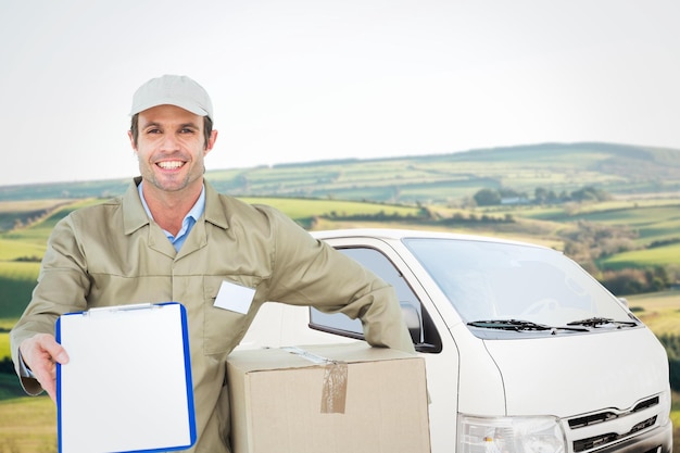 Repartidor feliz con caja que muestra portapapeles contra paisaje escénico