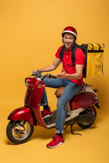 Foto repartidor feliz con mochila en scooter sobre fondo amarillo