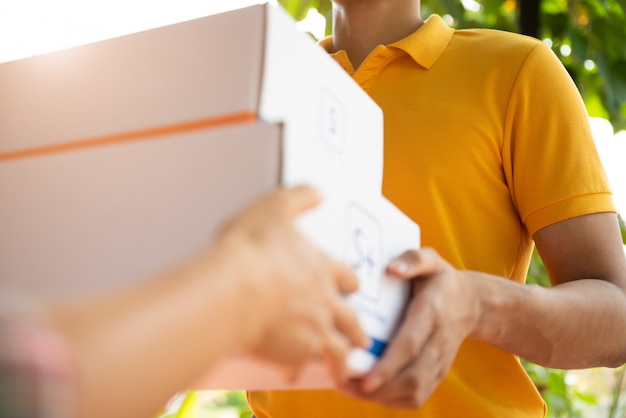 Repartidor feliz en uniforme de polo amarillo con caja de paquetería en las manos