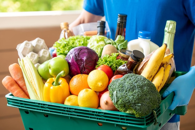 Repartidor con guantes sosteniendo una cesta de comestibles para un servicio higiénico de entrega de alimentos en el momento del concepto de pandemia