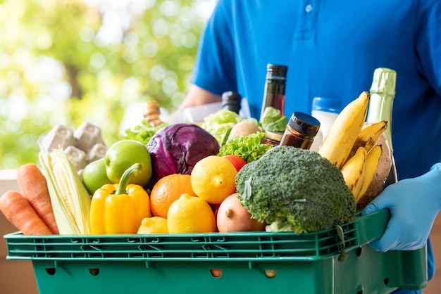 Repartidor con guantes sosteniendo una cesta de comestibles para un servicio higiénico de entrega de alimentos en el momento del concepto de pandemia