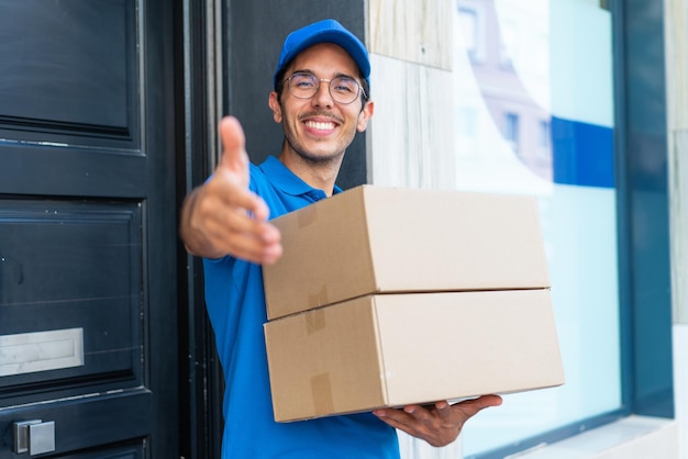 Repartidor joven al aire libre sosteniendo cajas con expresión feliz haciendo un trato