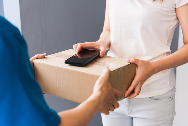 Repartidor joven asiático repartidor comprando en línea con buzón de paquetes en uniforme con mascarilla protectora haciendo servicio mujer cliente usando la firma del dedo de la mano en el teléfono móvil digital en casa