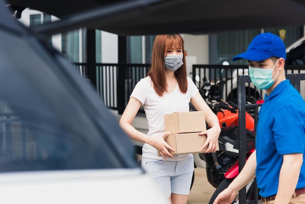 Repartidor joven asiático repartidor comprando en línea entrega el buzón del paquete el servicio de mascarilla protectora mujer cliente recibiendo caja en el frente de la casa, bajo toque de queda cuarentena pandemia coronavirus COVID-19