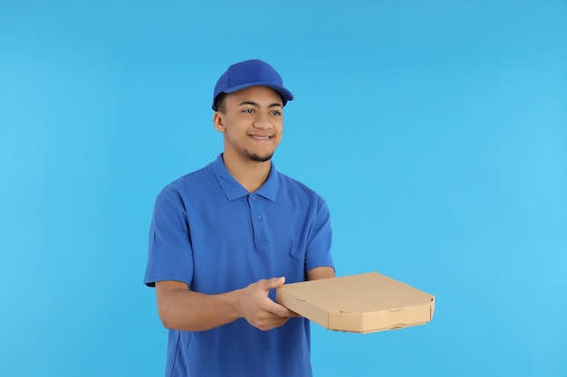 Repartidor joven con caja de pizza sobre fondo azul.