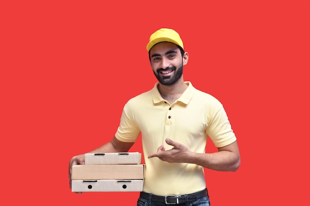 Repartidor joven mirada frontal en camiseta amarilla y sosteniendo cajas de pizza modelo paquistaní indio
