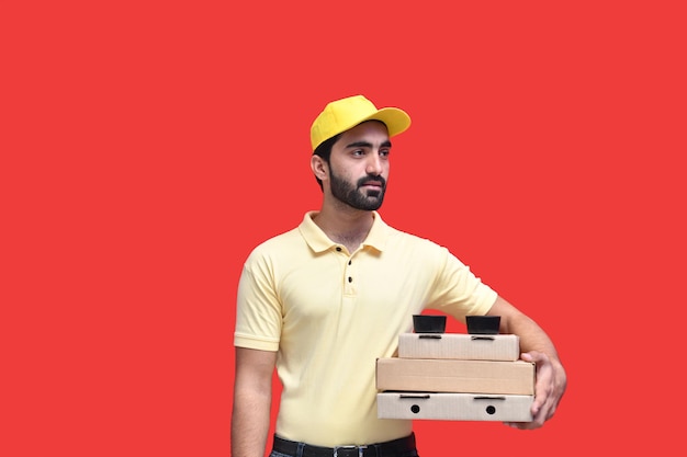 Repartidor joven mirando enfrente en camiseta amarilla sosteniendo 3 cajas de pizza modelo paquistaní indio