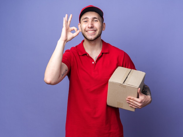 Repartidor joven sonriente vistiendo uniforme con caja de sujeción de tapa mostrando gesto bien