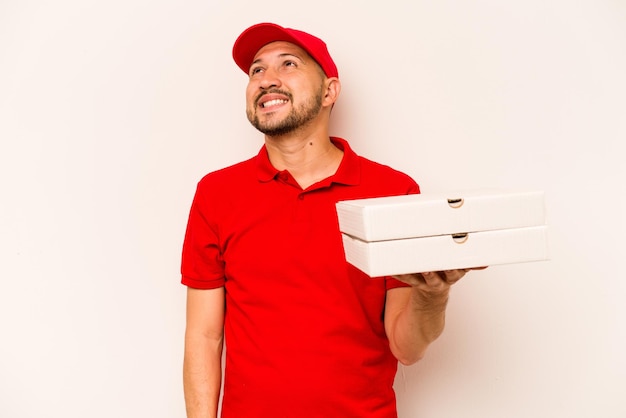 Repartidor joven sosteniendo pizzas aisladas sobre fondo beige soñando con lograr objetivos y propósitos