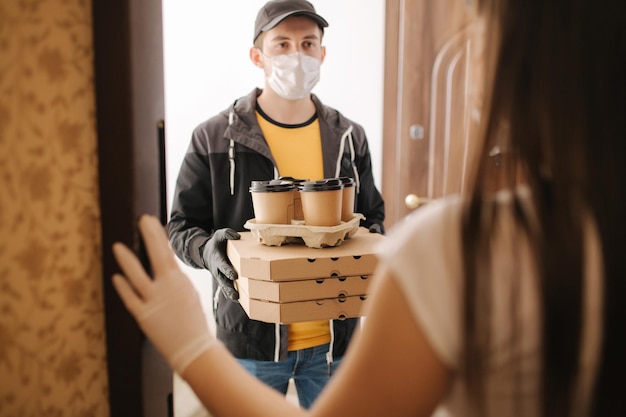 El repartidor con máscara y guantes le da pizza y café al cliente Quédese en casa