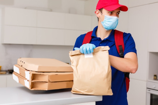 Foto repartidor con máscara médica protectora con caja de pizza: días de virus y pandemia, entrega de alimentos a su hogar.