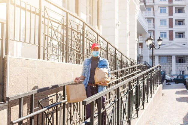 Repartidor en máscara protectora cerca de la casa del cliente, al aire libre