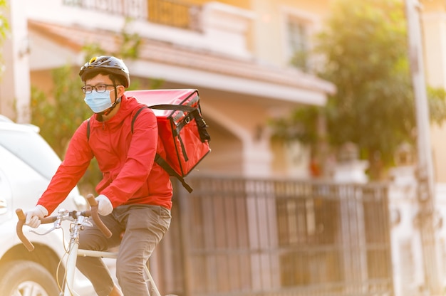 Repartidor con máscara protectora para evitar el virus corona uniforme rojo Ciclismo para entregar productos a los clientes en casa.