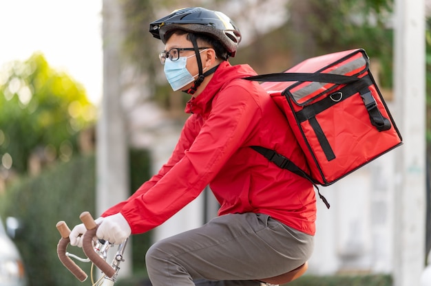 Repartidor con máscara protectora para evitar el virus corona uniforme rojo Ciclismo para entregar productos a los clientes en casa.