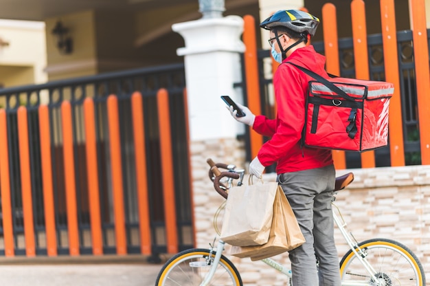 Repartidor con máscara protectora para evitar el virus corona uniforme rojo Ciclismo para entregar productos a los clientes en casa.