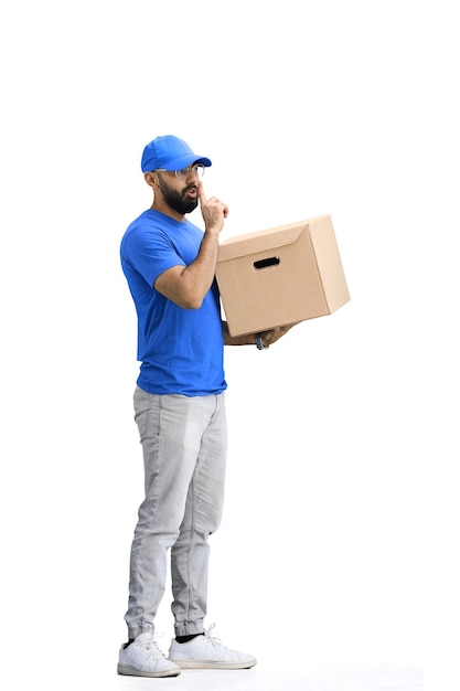 Un repartidor masculino en un fondo blanco a plena altura con una caja muestra un signo de silencio