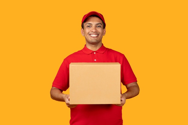Repartidor mexicano sosteniendo una caja dando un paquete sobre fondo amarillo