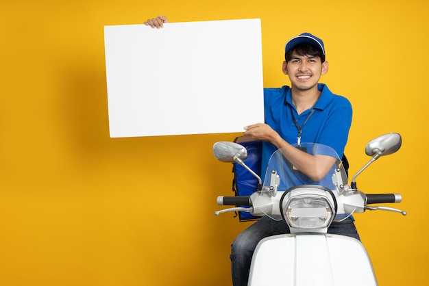 Foto repartidor montando motocicleta y mostrando pancarta blanca en blanco aislada sobre fondo amarillo