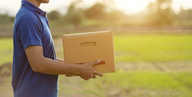 Repartidor con paquete marrón o cajas de cartón entrega al cliente en el campo